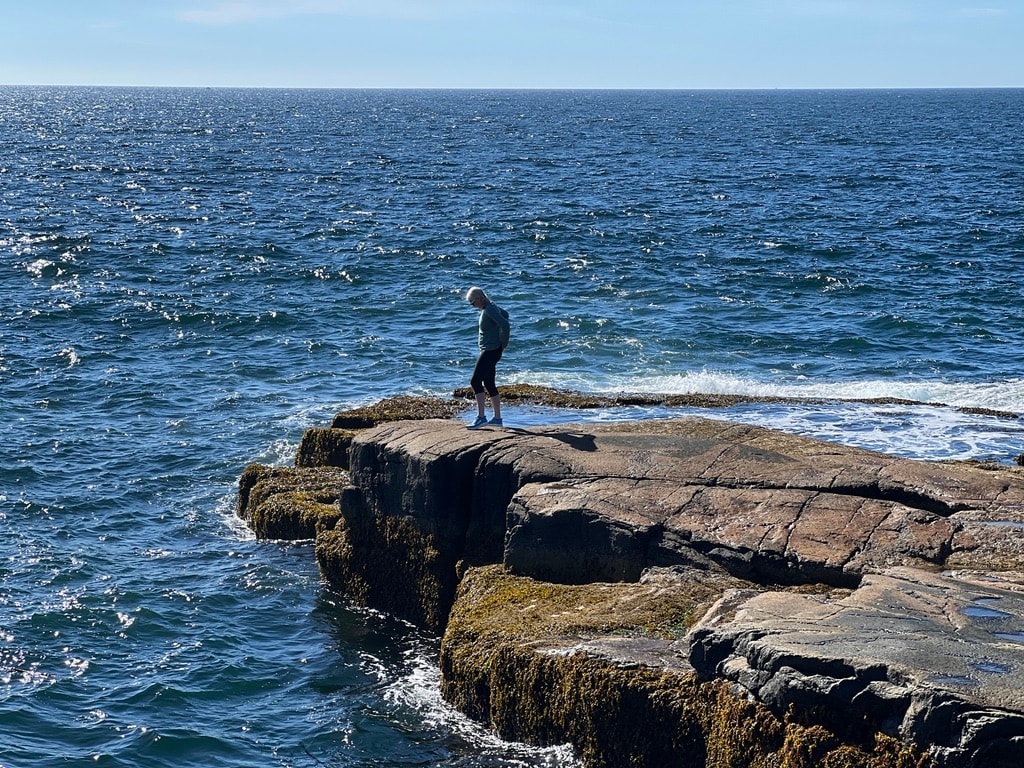 Katie on a rock in the ocean, from a distance